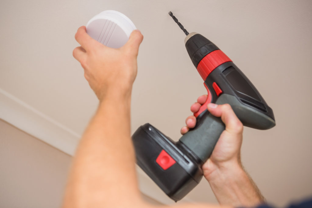 Handyman installing smoke detector with power tool on the ceiling